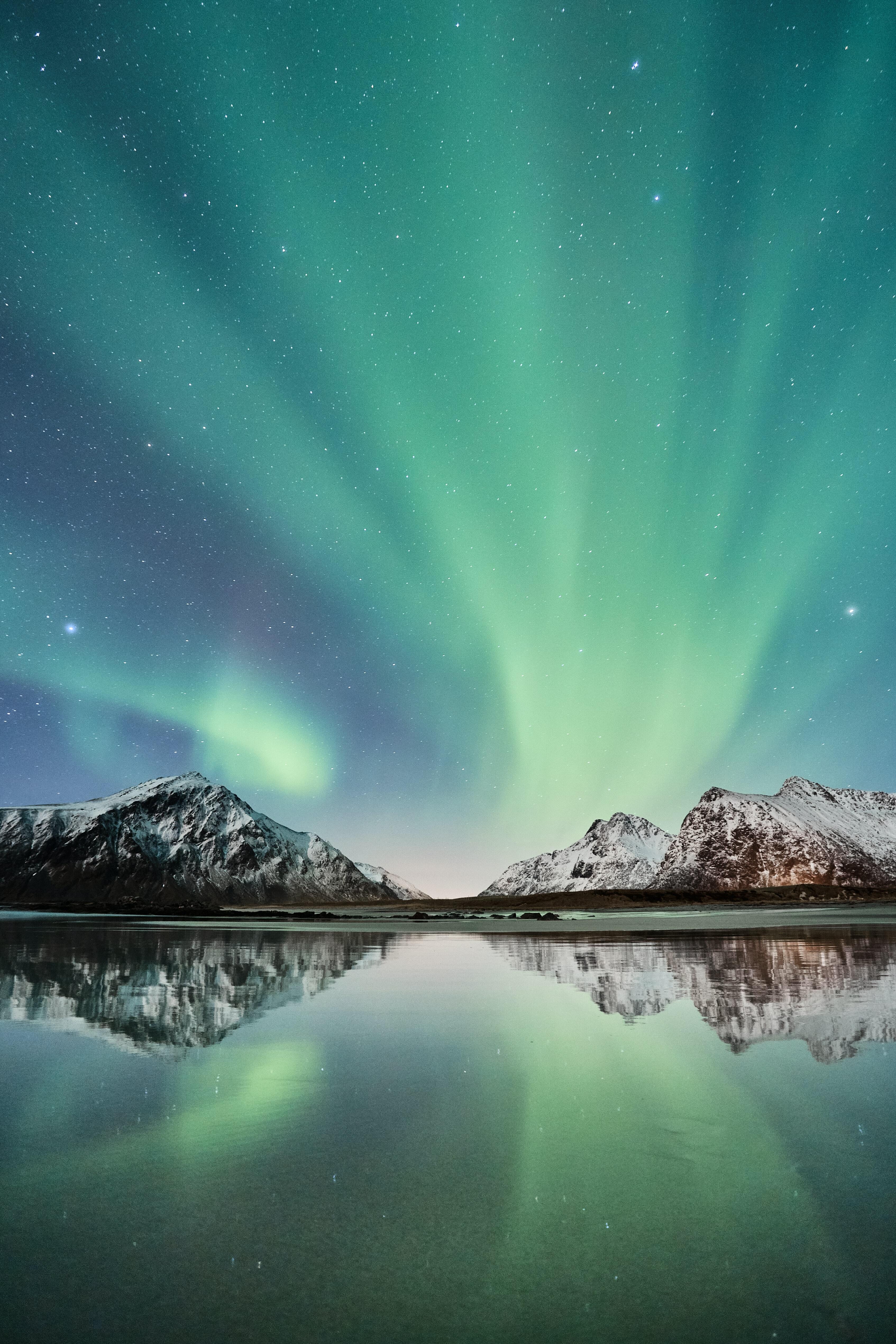 Grønt nordlys på kveldshimmel med fjell og refleksjon i vann. Foto: Unsplash.com / Johny Goerend