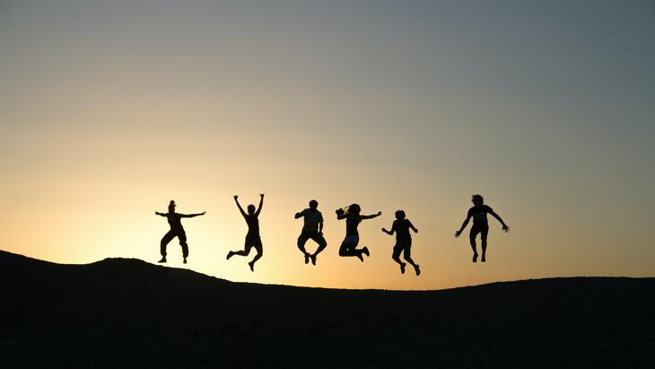 Gruppe av hoppende mennesker på et fjell i solnedgang. Foto: Unsplash.com / Timon Studler